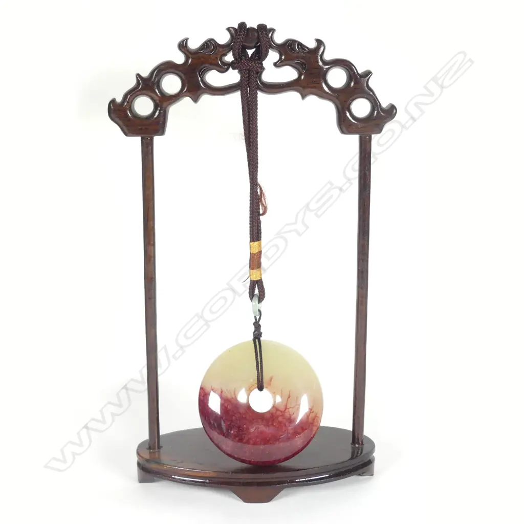 A Chinese chicken-blood jade disc suspended on wooden stand Image 1++