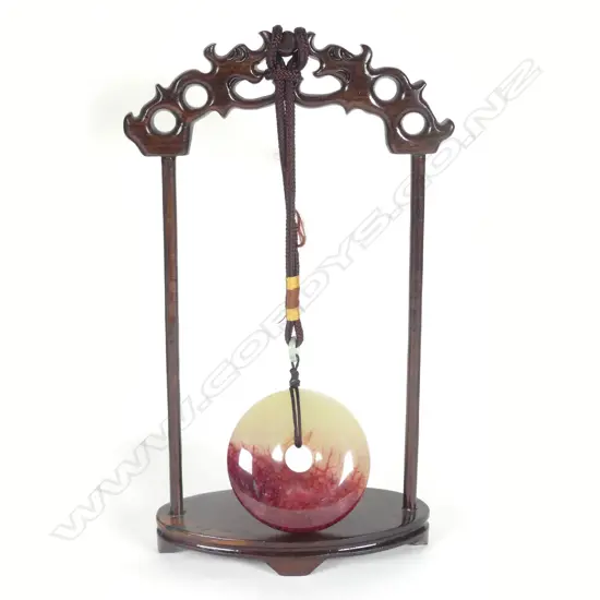 A Chinese chicken-blood jade disc suspended on wooden stand