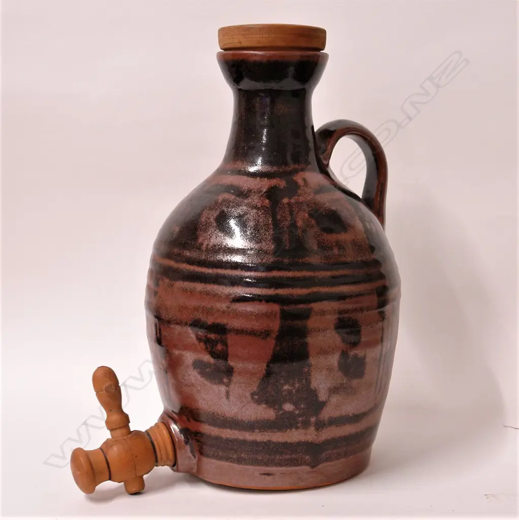 Crewenna Pottery (1962-1972 Harry & May Davis) flagon with dark tenmoku glaze - stylised decoration in lustrous dark red/brown tones, turned wooden topped cork stopper and tap. Potter's mark to base of strap handle. H.320mm. Image 1++