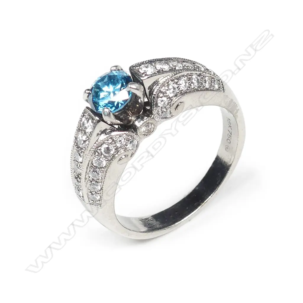An 18ct white gold treated blue diamond ring, the 'fancy colour' round brilliant cut diamond of 0.53ct in four claw tapered V setting flanked by a triple row of 42 grain set round brilliant cut diamonds, TDW 0.71ct. Valuation available. Image 1++