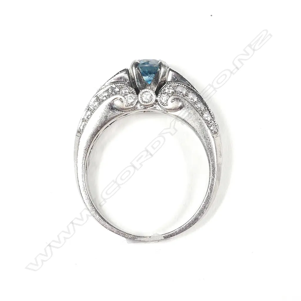 An 18ct white gold treated blue diamond ring, the 'fancy colour' round brilliant cut diamond of 0.53ct in four claw tapered V setting flanked by a triple row of 42 grain set round brilliant cut diamonds, TDW 0.71ct. Valuation available. Image 1++