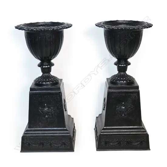 A pair of old refurbished cast iron urns on plinth bases,