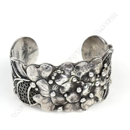 An uncommon Edith Morris Arts & Crafts silver cuff, this substantial studio jewellery item sculpted and applied with florals flanked by applied pierced panels and curved and scrolling bars, of solid construction. Impressed arrow and silver marks. W.34mm, Dia.65mm, 73gm. Note: Edith Morris arrived in New Zealand from Kent, England in 1924. She took a metalwork course at Wellington Technical College, where under the head of the college's School of Art, Nelson Isaac, she was taught jewellery, enamelling, chasing, repousse and silversmithing. From 1936 Morris worked from her studio/home in the artistic hub of Days Bay Wellington through until the early 1960's.