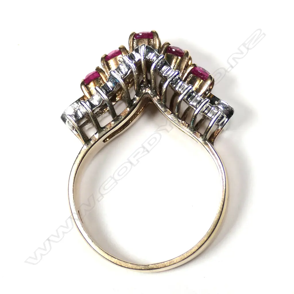 A retro 18ct gold ruby and diamond ring, the exaggerated V-form mount set with five round facet cut rubies framed by 22 small diamonds, 2 absent. Image 1++