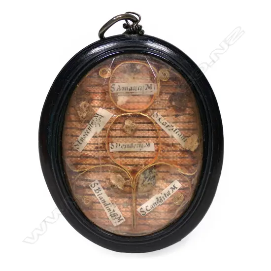 A portable reliquary in the form of a pendant, double sided with particular saints' minute body remains under faceted glass in a jet frame.  34 x 55mm.