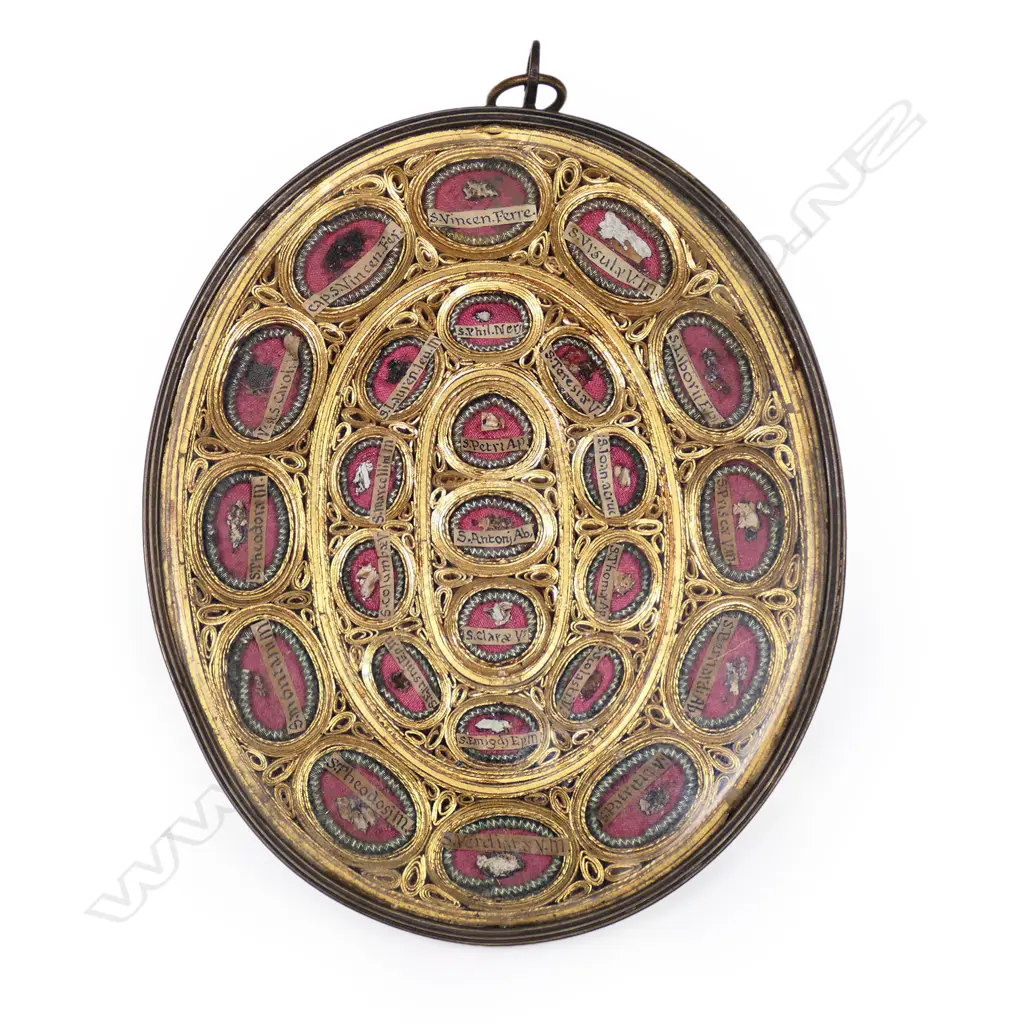 A portable reliquary, a brass frame enclosing braided gilt sections each containing particular saints' minute body remains, under glass. 115 x 140mm. Image 1++