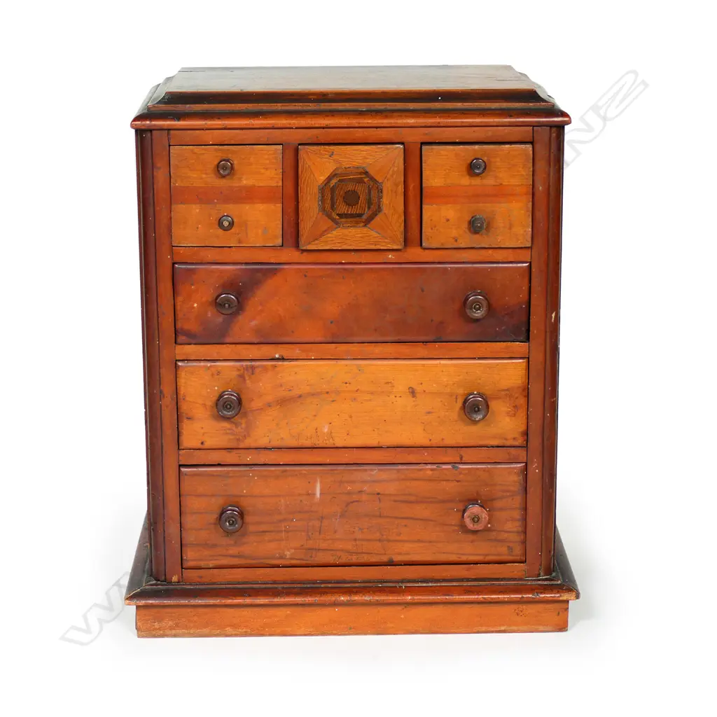A New Zealand native timbers miniature scotch chest, kauri, puriri, rewarewa and other timbers, the central top drawer with concealed spring latch/release. Four handles damaged or replaced. 290 x 180 x 350mm. Image 1++