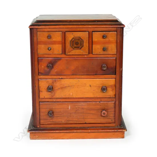 A New Zealand native timbers miniature scotch chest, kauri, puriri, rewarewa and other timbers, the central top drawer with concealed spring latch/release. Four handles damaged or replaced. 290 x 180 x 350mm.