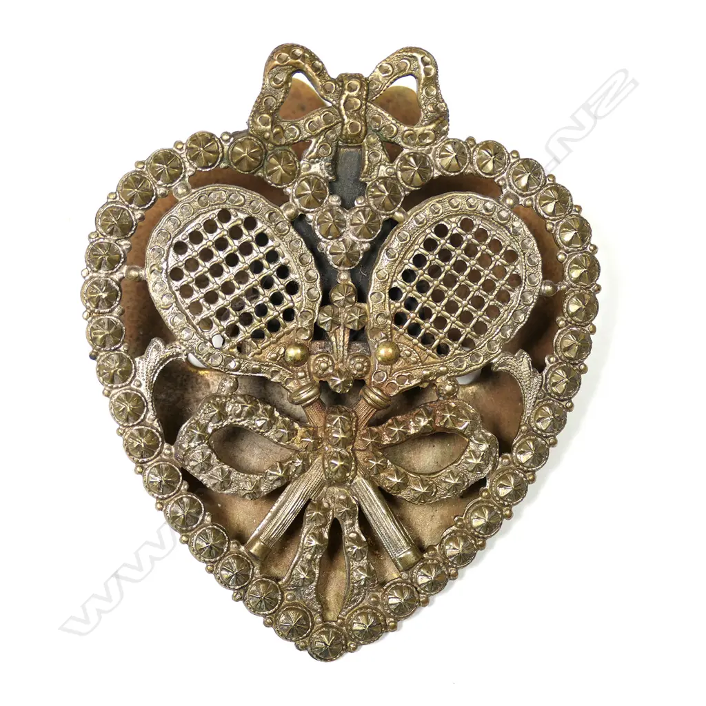 An Edwardian silver-plated brass tennis themed paper clasp, heart form, pierced and cast with crossed rackets tied with a bow. The silver plate showing the brass. H.78mm. Image 1++