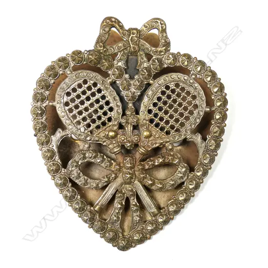An Edwardian silver-plated brass tennis themed paper clasp, heart form, pierced and cast with crossed rackets tied with a bow. The silver plate showing the brass. H.78mm.