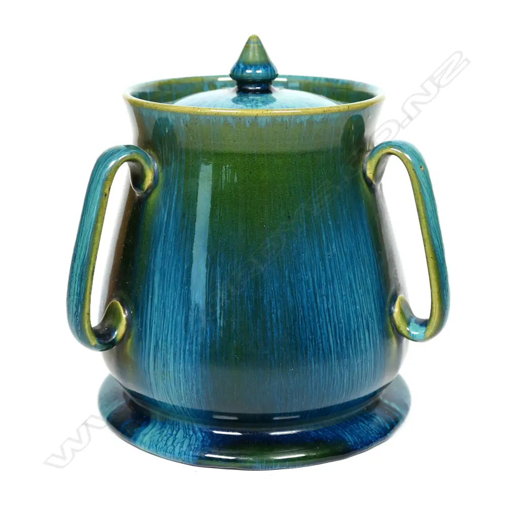 An Ashby Guild pottery lidded barrel, tapering shape on circular spreading foot, three elongated loop handles to the side. Streaked tonal blue green glaze. Impressed stamp. H.170mm Image 1++