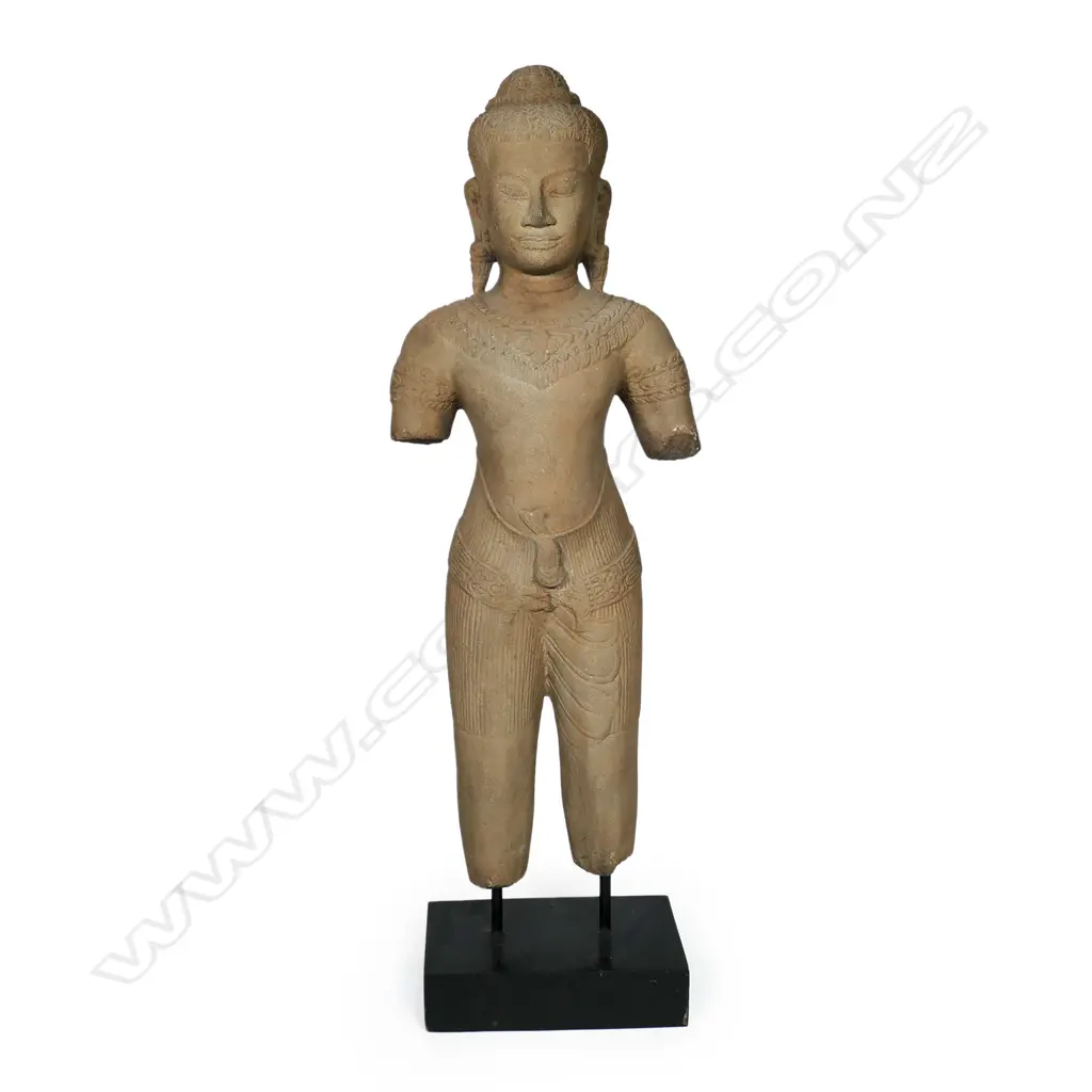 A 20thC Khmer inspired statue of a female divinity, finely detailed, with serene face, almond shaped eyes below her arched brow. Long pendulous pierced earlobes, finely braided tresses and secured by a braided band with a mango leaf shaped accent. Raised on ebonised rectangular stand. H.715mm. Image 1++