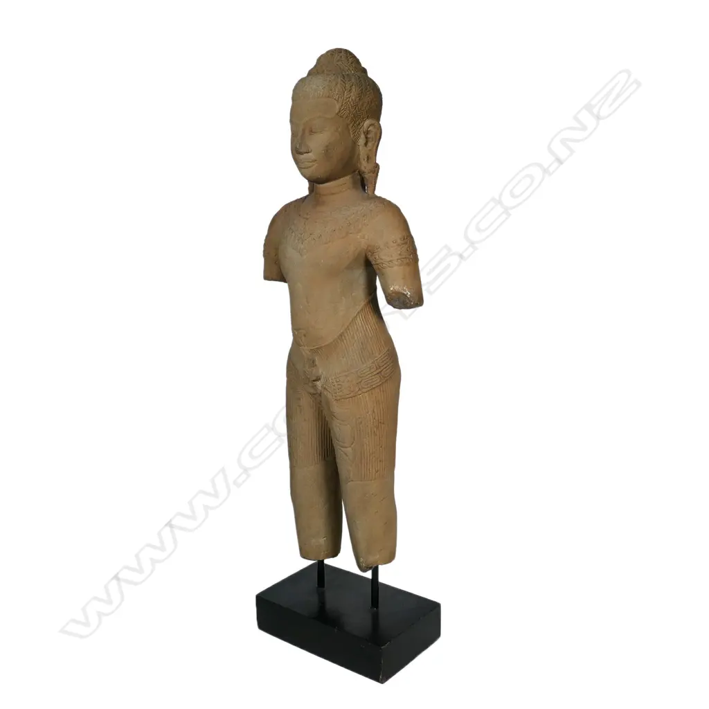 A 20thC Khmer inspired statue of a female divinity, finely detailed, with serene face, almond shaped eyes below her arched brow. Long pendulous pierced earlobes, finely braided tresses and secured by a braided band with a mango leaf shaped accent. Raised on ebonised rectangular stand. H.715mm. Image 1++