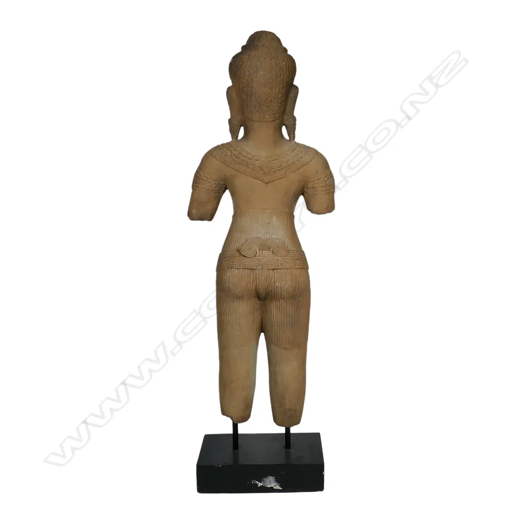 A 20thC Khmer inspired statue of a female divinity, finely detailed, with serene face, almond shaped eyes below her arched brow. Long pendulous pierced earlobes, finely braided tresses and secured by a braided band with a mango leaf shaped accent. Raised on ebonised rectangular stand. H.715mm. Image 1++