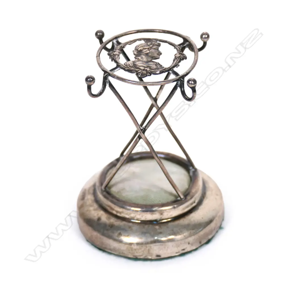An Edwardian silver hat pin cushion stand, the top with the portrait bust of a maiden in profile. Chester 1908. H.74mm. Image 1++