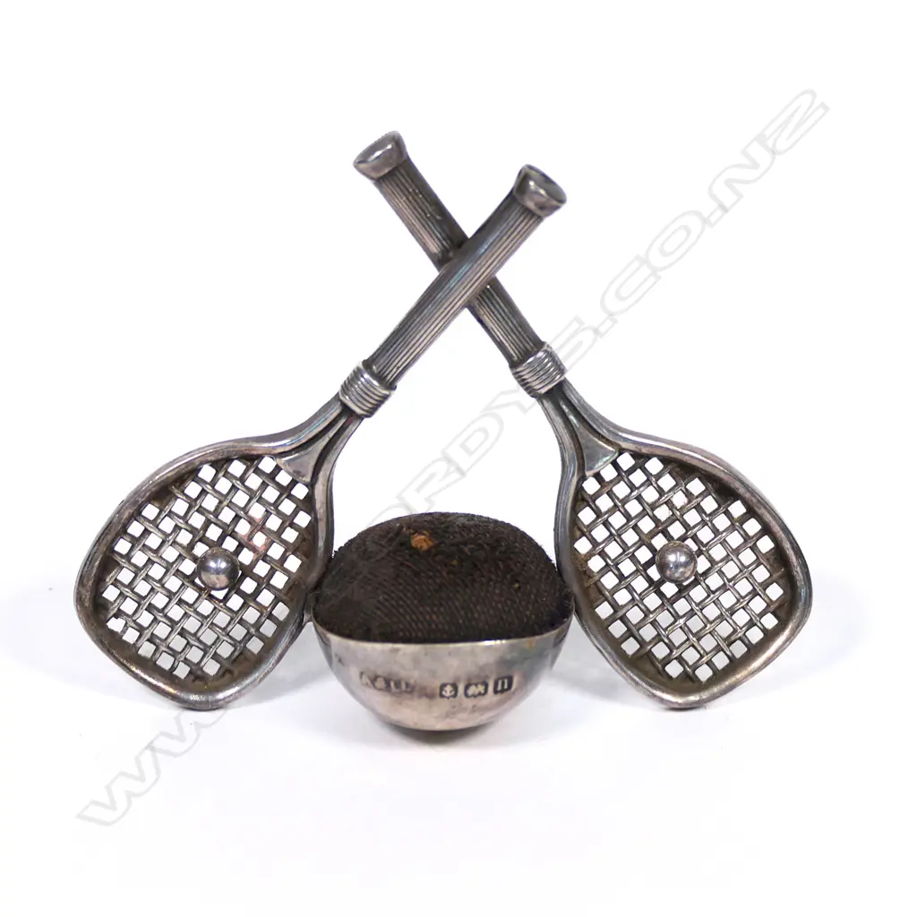 An early 20thC rare silver tennis themed pin cushion, the stand as two crossed rackets centred with balls flanking the cushion. Birmingham 1912. By Adie & Lovekin Ltd. H.50mm. Image 1++