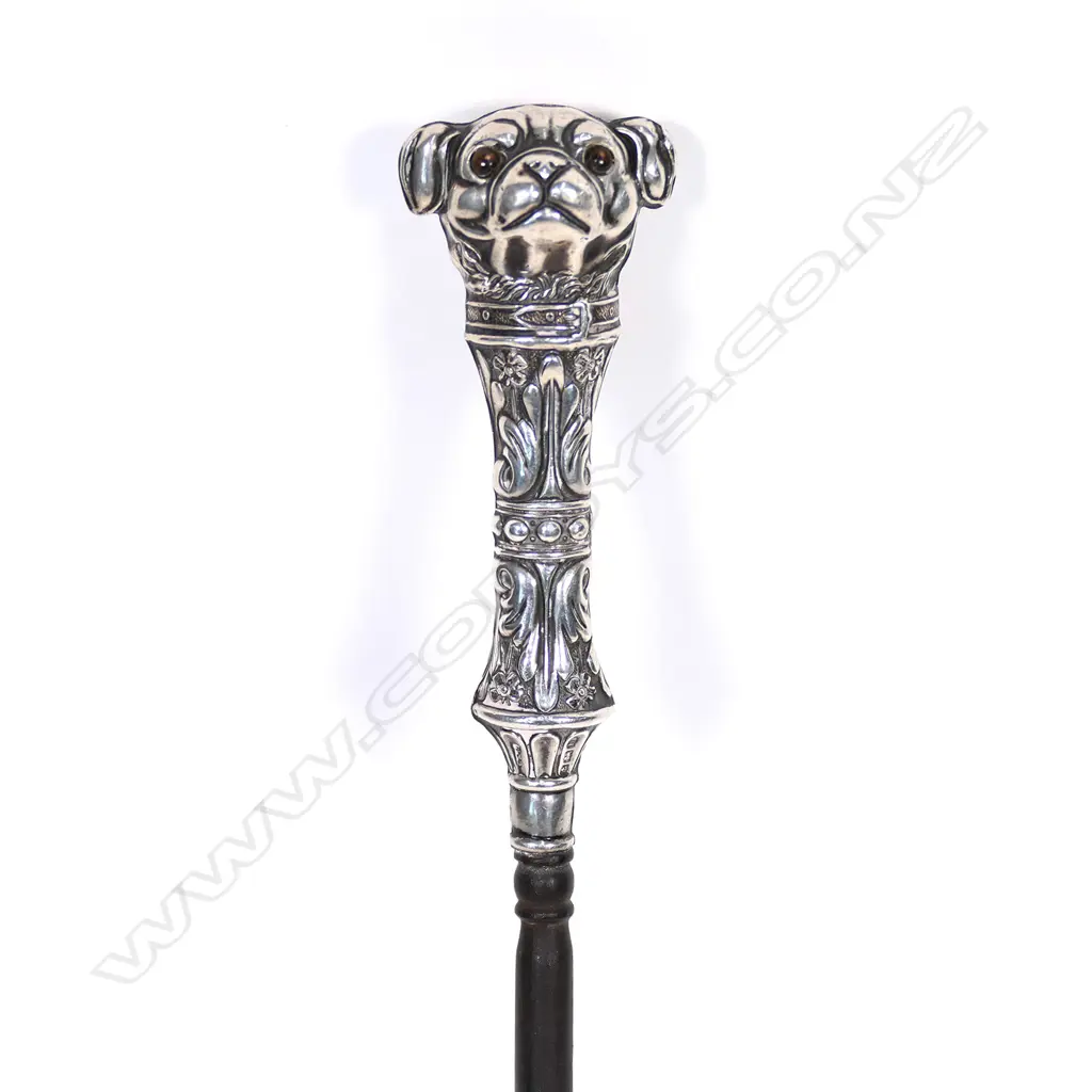 An uncommon Edwardian silver dog handled boot hook, the pug type dog with glass eyes, with collar and leafy and floral bands, steel shaft. L.230mm. Birmingham 1907, by Crisford & Norris Ltd. Minor faults consistent with age. Image 1++