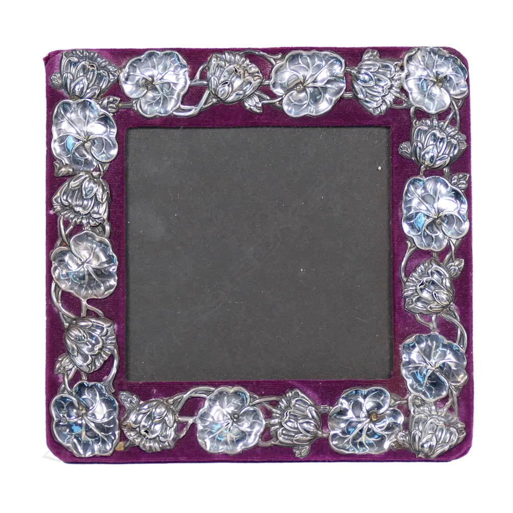 An Edwardian silver Art Nouveau photo frame, waterlily leaf and flower repeating embossed border on maroon velvet. Velvet back with wooden strut. 180 x 185mm. Birmingham 1902 by William Devonport. Minor faults consistent with age. Image 1++