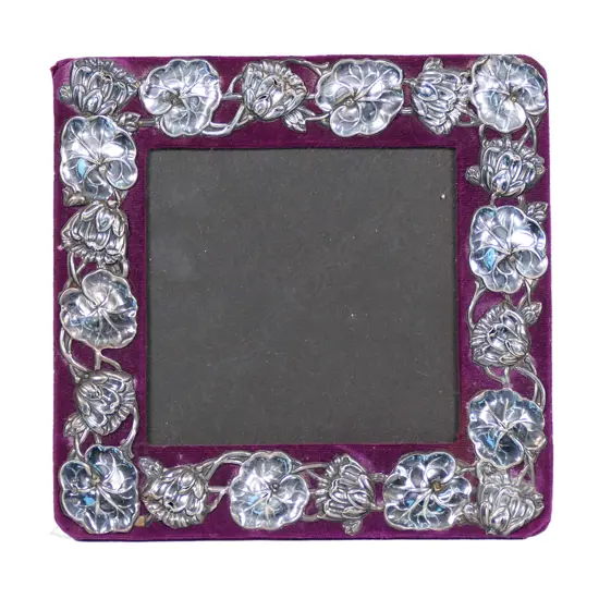 An Edwardian silver Art Nouveau photo frame, waterlily leaf and flower repeating embossed border on maroon velvet. Velvet back with wooden strut. 180 x 185mm. Birmingham 1902 by William Devonport. Minor faults consistent with age.
