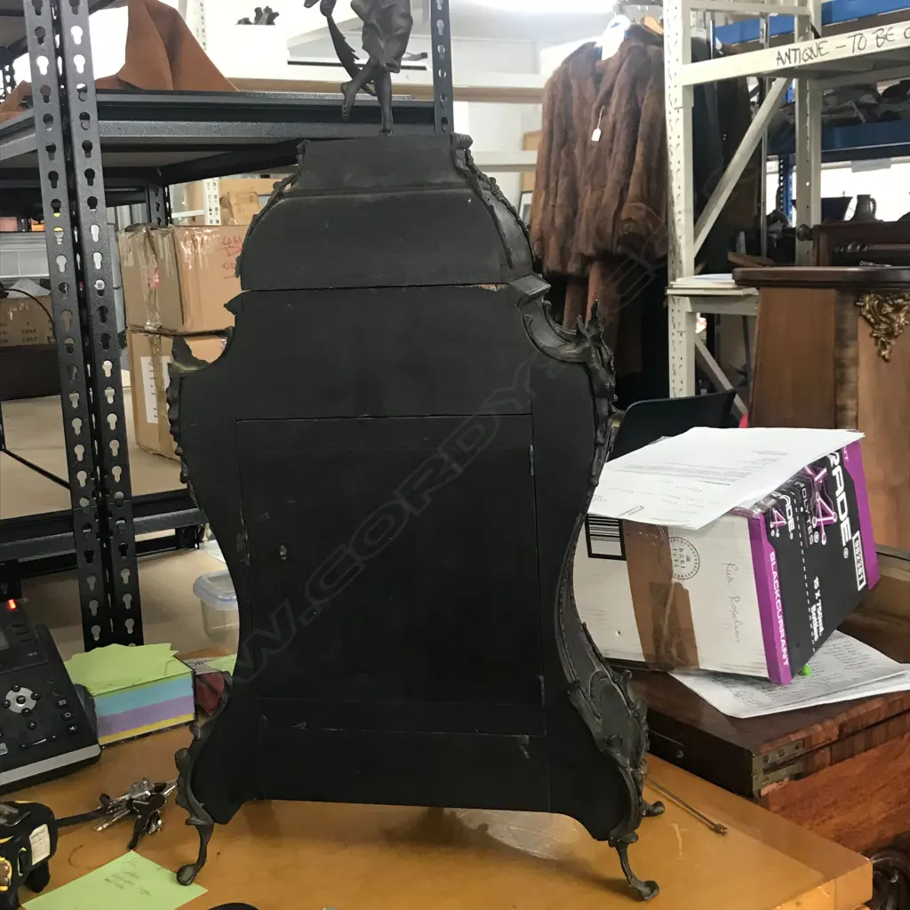 A Louis XVI-style mantel clock, the shaped case inlaid with cut brass Boulle work on black lacquered ground and heavily tarnished rococo ormolu mounts, surmounted by a pagoda top crowned by a standing heraldic angel figure. The cast dial with white enamel hour cartouches with blue Roman numerals, gong striking movement, sunburst pendulum above a sloping checkered floor, behind a glazed door mounted with a floral adorned putti. H.640mm. Image 1++