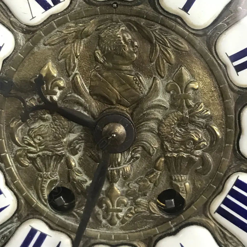 A Louis XVI-style mantel clock, the shaped case inlaid with cut brass Boulle work on black lacquered ground and heavily tarnished rococo ormolu mounts, surmounted by a pagoda top crowned by a standing heraldic angel figure. The cast dial with white enamel hour cartouches with blue Roman numerals, gong striking movement, sunburst pendulum above a sloping checkered floor, behind a glazed door mounted with a floral adorned putti. H.640mm. Image 1++