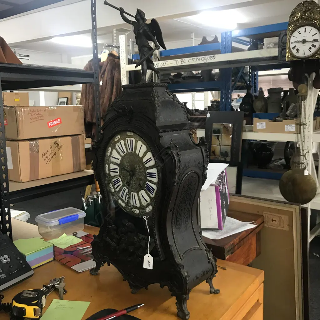 A Louis XVI-style mantel clock, the shaped case inlaid with cut brass Boulle work on black lacquered ground and heavily tarnished rococo ormolu mounts, surmounted by a pagoda top crowned by a standing heraldic angel figure. The cast dial with white enamel hour cartouches with blue Roman numerals, gong striking movement, sunburst pendulum above a sloping checkered floor, behind a glazed door mounted with a floral adorned putti. H.640mm. Image 1++