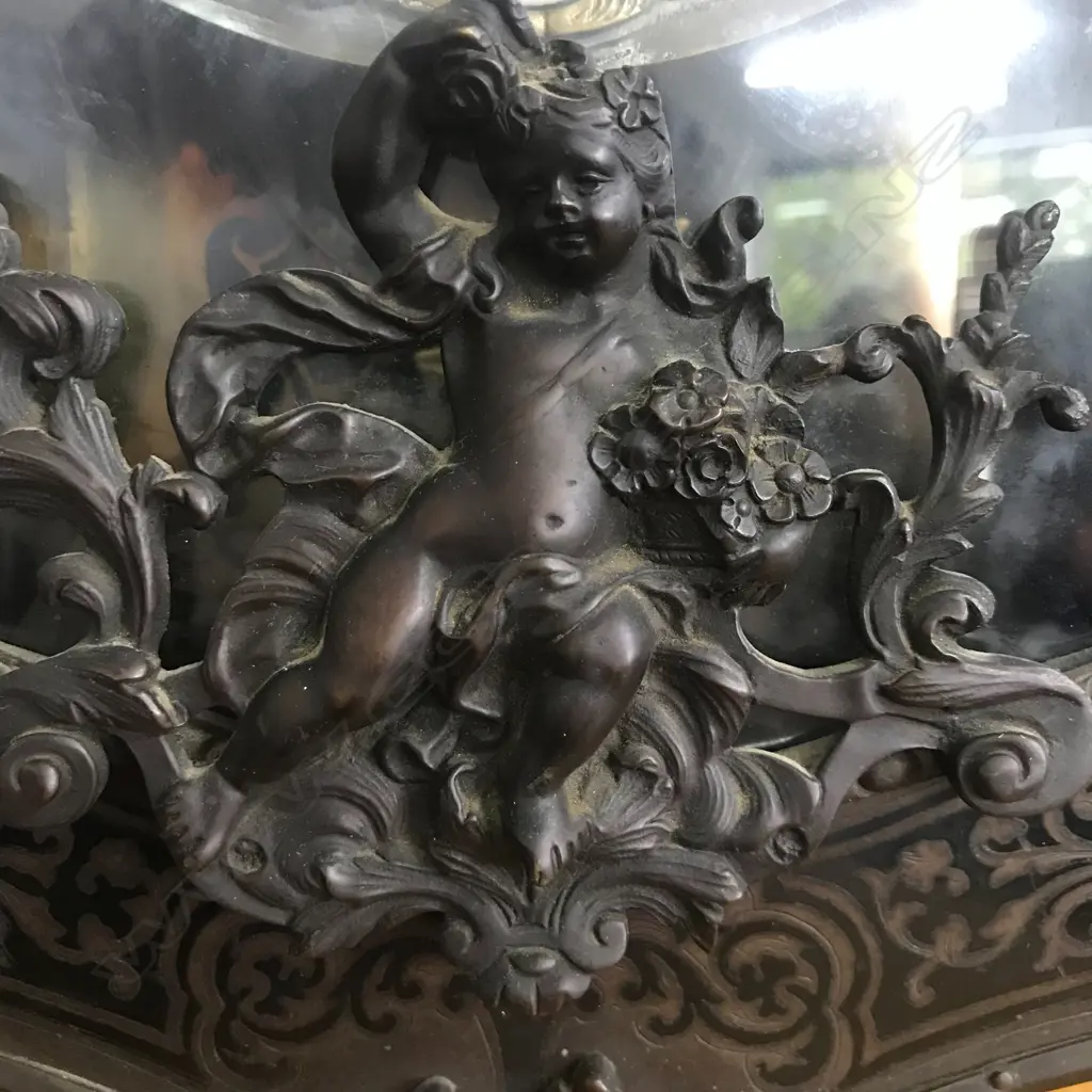 A Louis XVI-style mantel clock, the shaped case inlaid with cut brass Boulle work on black lacquered ground and heavily tarnished rococo ormolu mounts, surmounted by a pagoda top crowned by a standing heraldic angel figure. The cast dial with white enamel hour cartouches with blue Roman numerals, gong striking movement, sunburst pendulum above a sloping checkered floor, behind a glazed door mounted with a floral adorned putti. H.640mm. Image 1++