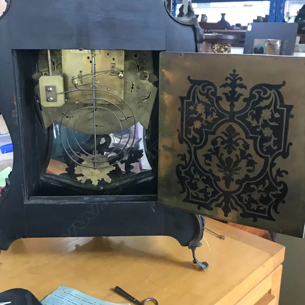 A Louis XVI-style mantel clock, the shaped case inlaid with cut brass Boulle work on black lacquered ground and heavily tarnished rococo ormolu mounts, surmounted by a pagoda top crowned by a standing heraldic angel figure. The cast dial with white enamel hour cartouches with blue Roman numerals, gong striking movement, sunburst pendulum above a sloping checkered floor, behind a glazed door mounted with a floral adorned putti. H.640mm. Image 1++