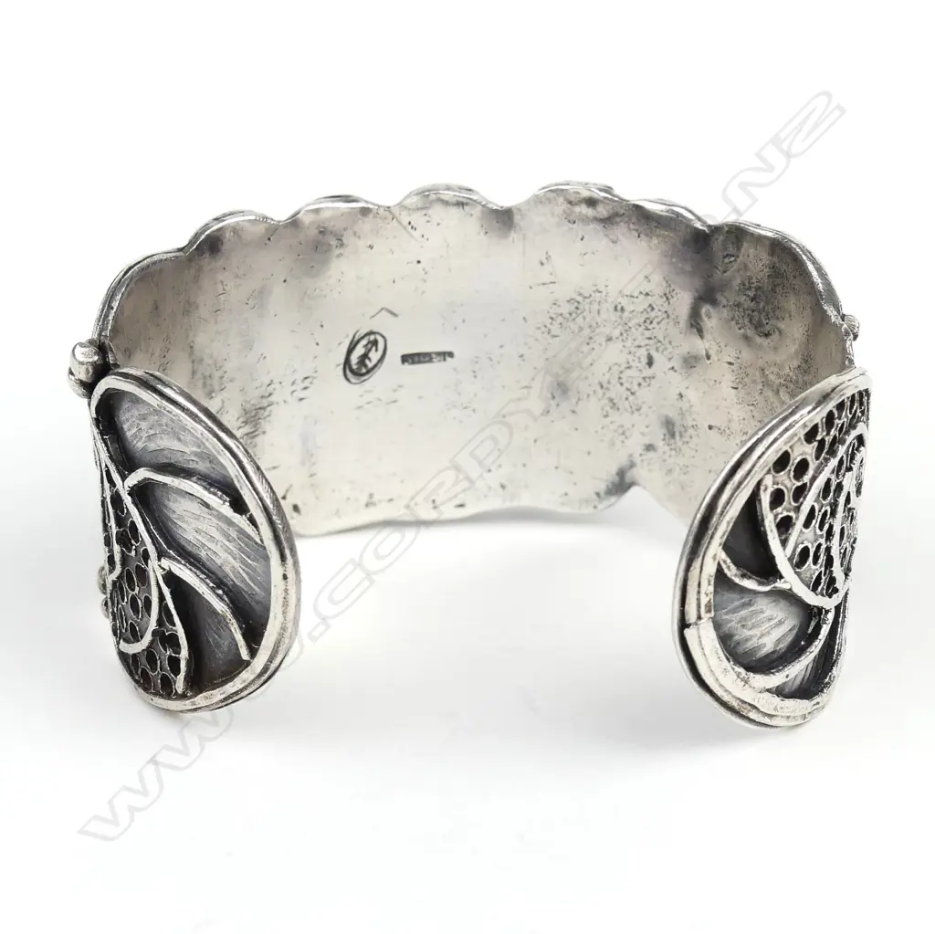 An uncommon Edith Morris Arts & Crafts silver cuff, this substantial studio jewellery item sculpted and applied with florals flanked by applied pierced panels and curved and scrolling bars, of solid construction. Impressed arrow and silver marks. W.34mm, Dia.65mm, 73gm. Note: Edith Morris arrived in New Zealand from Kent, England in 1924. She took a metalwork course at Wellington Technical College, where under the head of the college's School of Art, Nelson Isaac, she was taught jewellery, enamelling, chasing, repousse and silversmithing. From 1936 Morris worked from her studio/home in the artistic hub of Days Bay Wellington through until the early 1960's. Image 1++