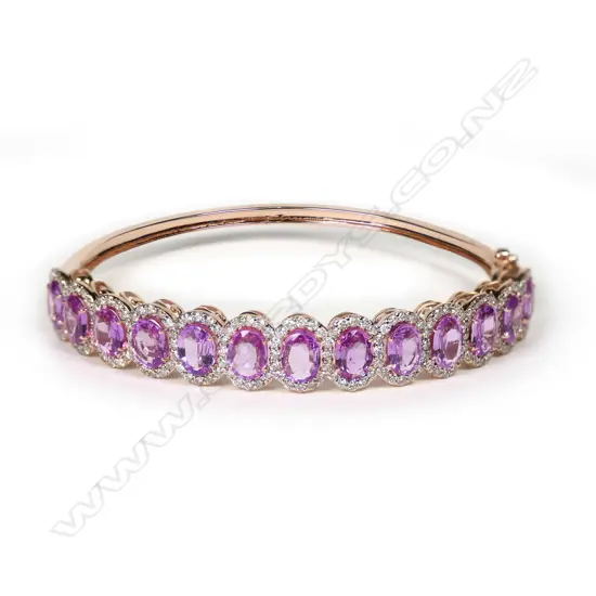 A 14ct rose gold pink sapphire and diamond halo bangle, thirteen oval cut pink sapphires (eye clean to slightly included), claw set, each surrounded by a halo of round brilliant cut diamonds (J-M/champagne colour, SI1-I2 clarity), hinged closure with safety catch, TSW 10.27ct, TDW  1.98ct.