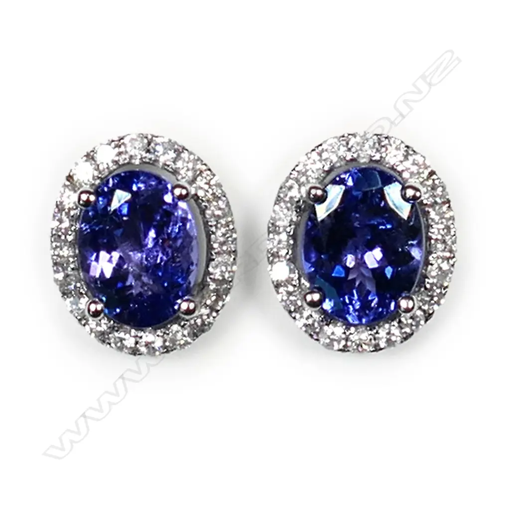 A pair of 14ct white gold tanzanite and diamond halo earrings, each earring set with a 1.17ct oval cut violet blue tanzanite (moderate to heavy inclusions), claw set and surrounded by twenty round brilliant cut diamonds (colour G-J, clarity I1-I2), posts for pierced ears, TTW 2.35ct, TDW 0.38ct. Image 1++