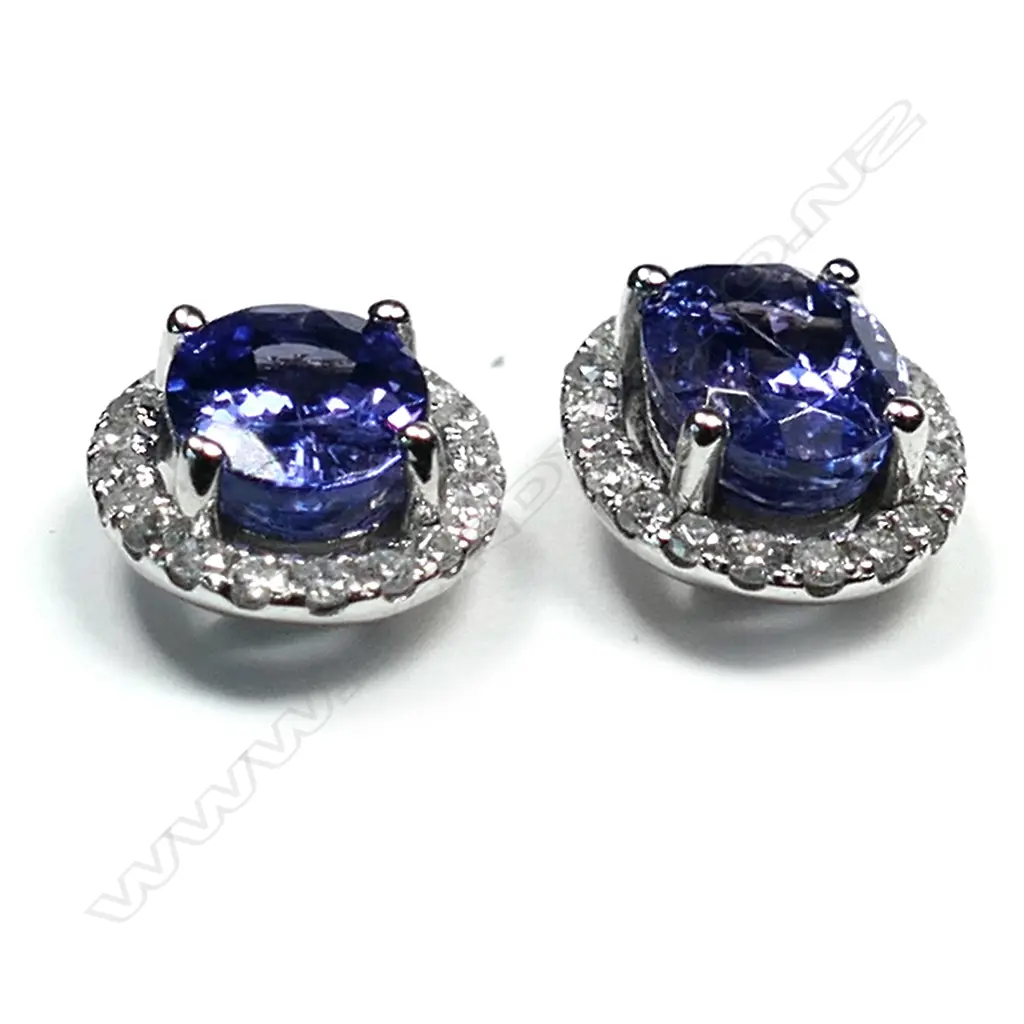 A pair of 14ct white gold tanzanite and diamond halo earrings, each earring set with a 1.17ct oval cut violet blue tanzanite (moderate to heavy inclusions), claw set and surrounded by twenty round brilliant cut diamonds (colour G-J, clarity I1-I2), posts for pierced ears, TTW 2.35ct, TDW 0.38ct. Image 1++