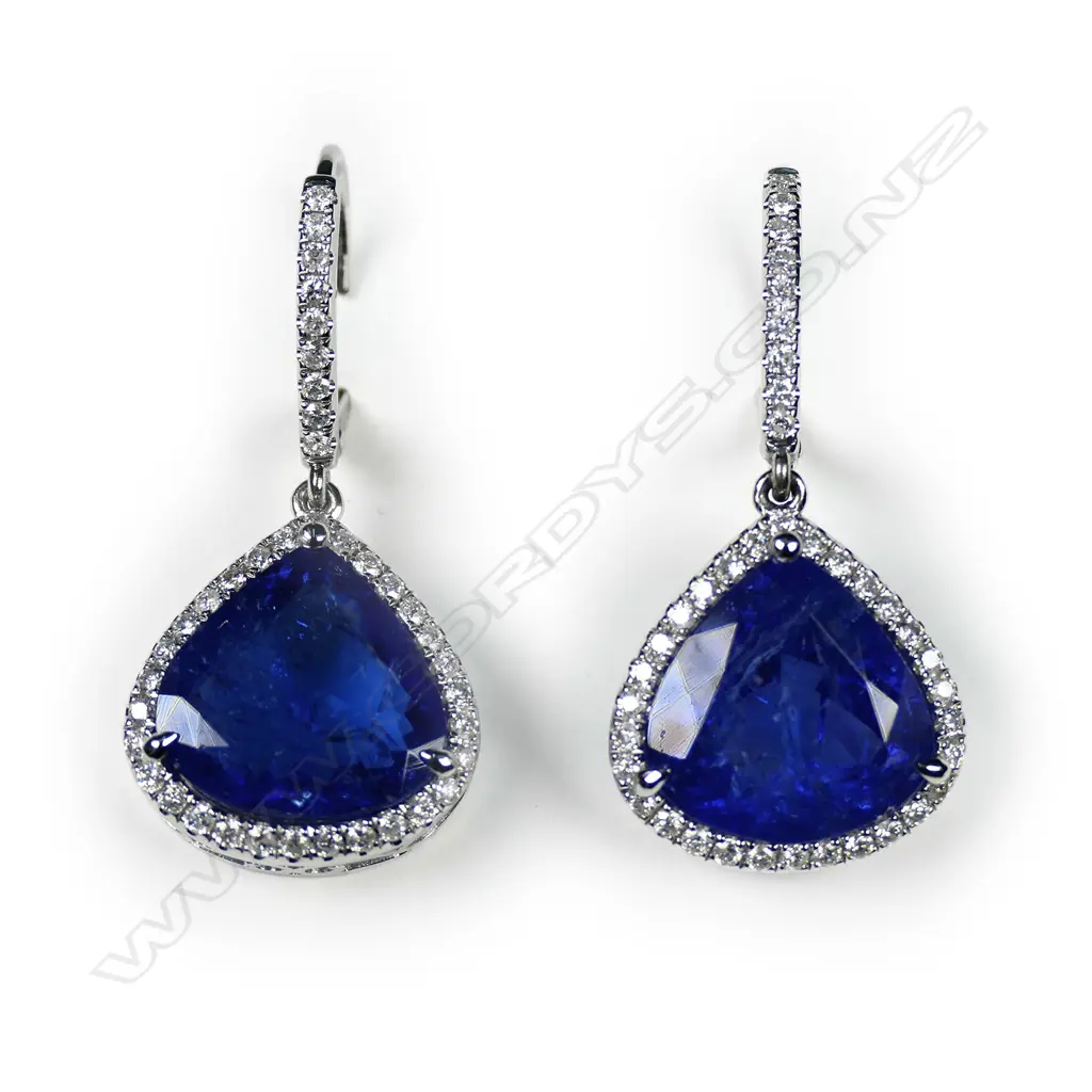 A pair of 14ct white gold tanzanite and diamond halo drop earrings, each earring set with a 5.82ct pear cut purplish-blue tanzanite (eye visible inclusions), claw set, surrounded by thirty-nine round brilliant cut diamonds (H-I colour, SI2-I2 clarity), lever backs for pierced ears, TTW 11.64ct TDW 0.63ct. Image 1++