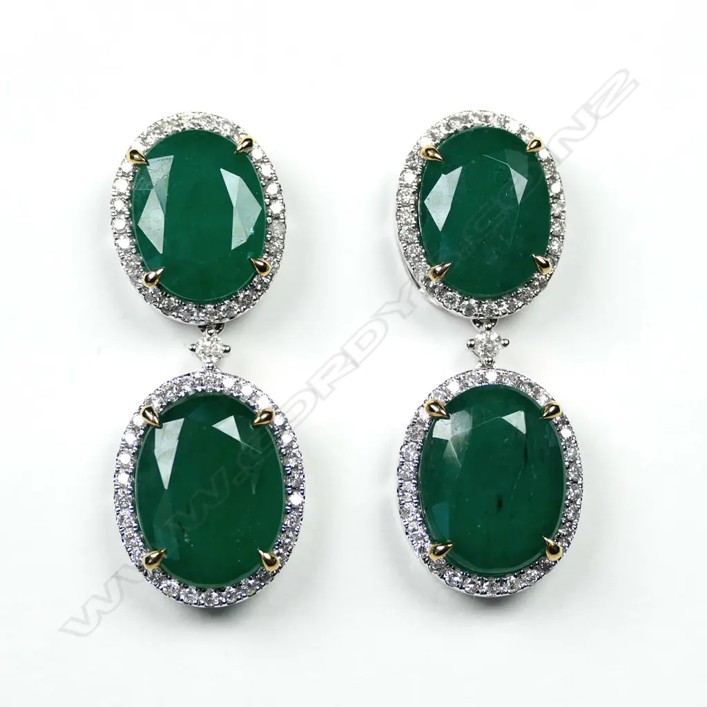A pair of 14ct white gold emerald and diamond drop halo earrings, each earring set with two oval cut, bluish green Zambian emeralds (eye visible inclusions), claw set in yellow gold, each surrounded by a halo of round brilliant cut diamonds (G-H colour, SI1-I2 clarity), posts for pierced ears, TEW 19.59ct, TDW 0.91ct. Image 1++