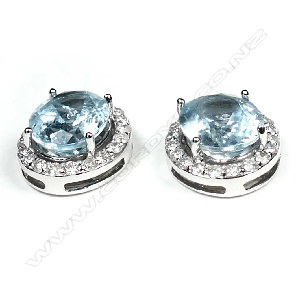 A pair of 14ct white gold aquamarine and diamond halo stud earrings, each earring set with a 2.18ct oval cut light blue aquamarine (eye clean clarity), claw set and surrounded by twenty round brilliant cut diamonds (H-I colour, SI2-I1 clarity), posts for pierced ears, TAW 4.36ct, TDW  0.58ct. Image 1++