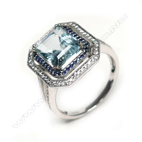 A 14k white gold aquamarine diamond and sapphire ring, the octagonal cut 3.13ct aquamarine framed by rows of small sapphires and diamonds, further diamonds to the forked shoulders. With AIG certificate and valuation available.