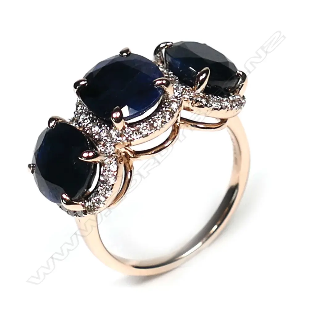 A 14ct rose gold sapphire and diamond halo trilogy ring, three oval cut dark blue sapphires (slightly included), claw set, each sapphire surrounded by a halo of round brilliant cut diamonds (J-M colour, SI1-P1 clarity), TSW 9.31ct, TDW 0.55ct, Ring Size O1/2. Image 1++