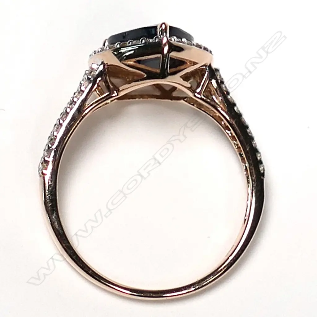 A 14ct rose gold sapphire and diamond halo ring, a 2.58ct pear cut dark blue sapphire (slightly included), claw set and surrounded by a halo of twenty-six round brilliant cut diamonds (J-M champagne colour, SI1-I2 clarity), with a further eighteen diamonds to the split shoulders, (J-M champagne colour, SI1-I2 clarity) TDW 0.34ct, ring size M 1/2. Image 1++