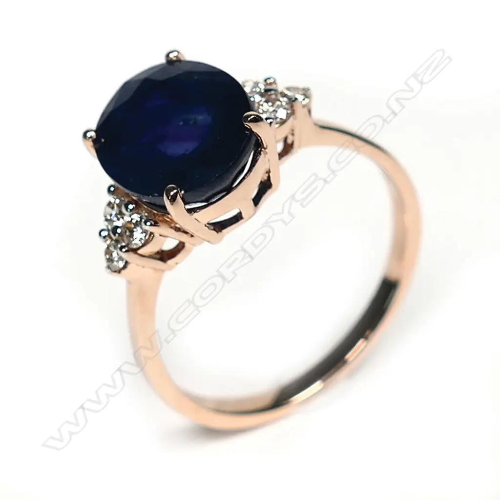 A 14ct rose gold sapphire and diamond ring, a 3.36ct oval cut dark blue sapphire (slightly included), claw set with three round brilliant cut champagne diamonds to each shoulder (0.18ct TDW, SI1-I1 clarity), ring size L. Image 1++