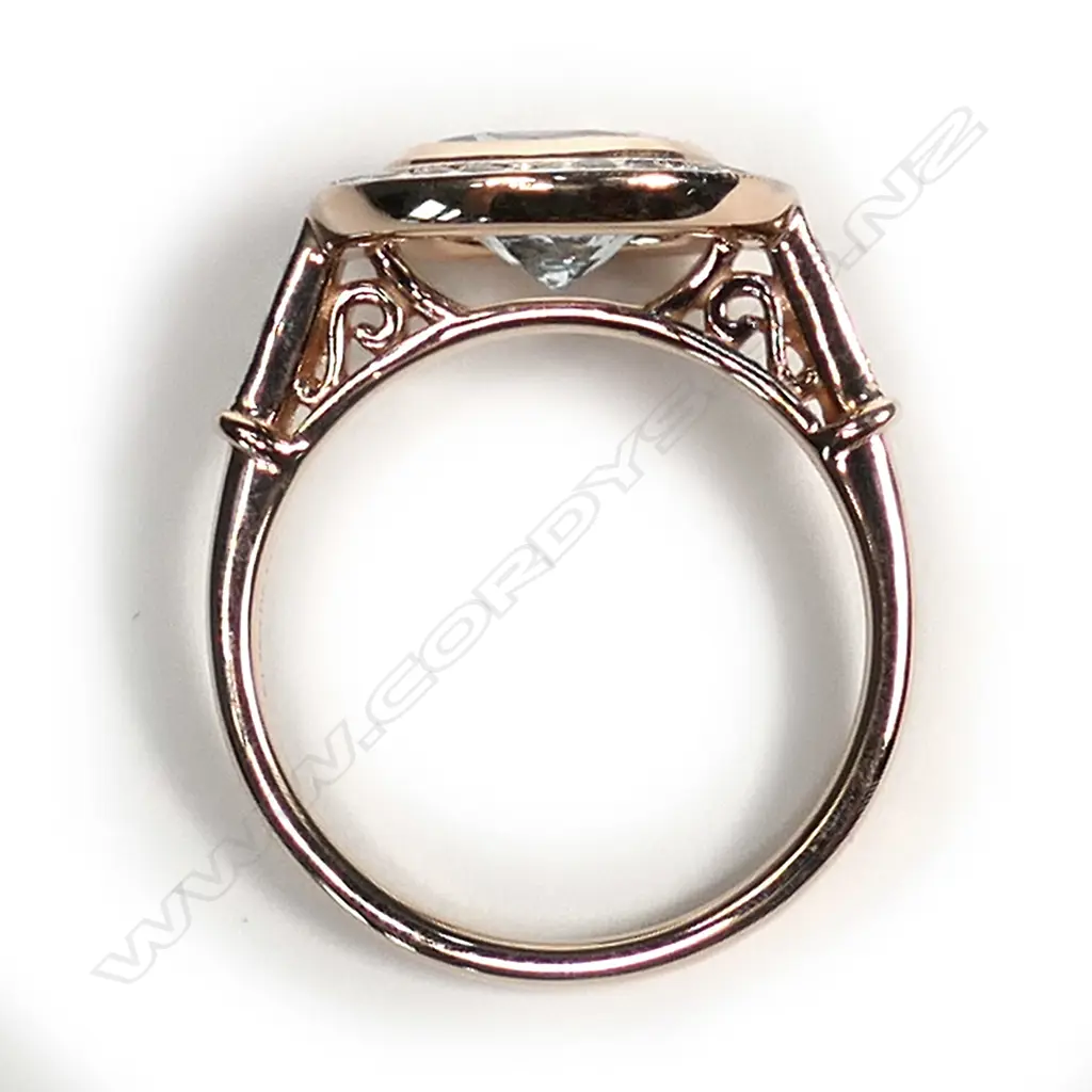 A 14ct rose gold aquamarine and diamond ring, a 1.75ct square cushion cut greyish-blue aquamarine (eye clean clarity), bezel set and surrounded by a halo of twenty-six round brilliant cut diamonds with a further three diamonds to each shoulder, (H-J colour, SI2-I2 clarity), TDW 0.43ct ring size N. Image 1++