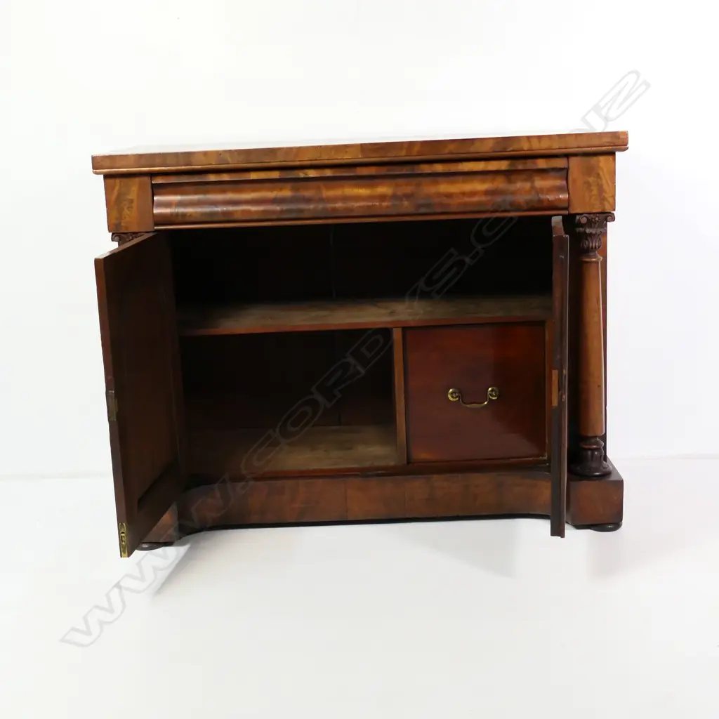 A Regency flame mahogany small sideboard/chiffonier, scrolling back, frieze drawer to the top with full Corinthian columns to each side of two panelled doors, raised on plinth base with squat bun feet.  (Sun fading to one side) 1230 x 575 x 1520mm. Note: This piece does have a scroll back, not shown in photo. Image 1++