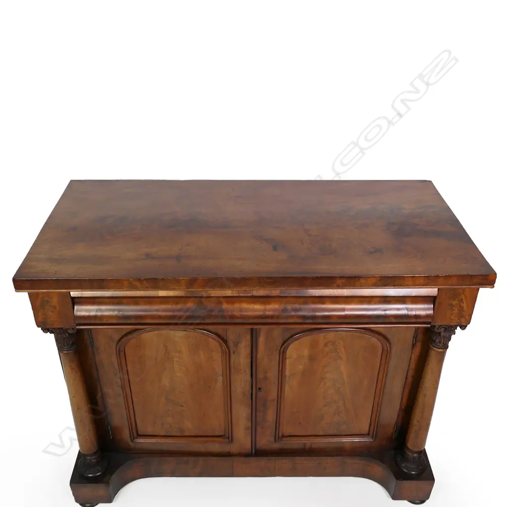 A Regency flame mahogany small sideboard/chiffonier, scrolling back, frieze drawer to the top with full Corinthian columns to each side of two panelled doors, raised on plinth base with squat bun feet.  (Sun fading to one side) 1230 x 575 x 1520mm. Note: This piece does have a scroll back, not shown in photo. Image 1++
