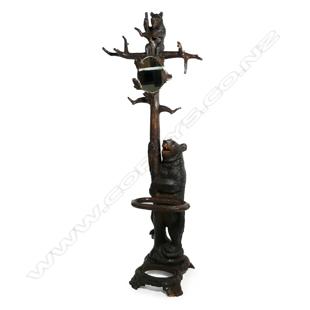 An early 1900s carved Black Forest bear hall/umbrella stand, the mother bear holding the tree trunk and with her cub perched on the top, oak leaf framed mirror to the centre, some evidence of old borer to the right hand side of the base, drip tray absent. (Together with a copy of 'Swiss Carvings, The Art of the Black Forest' which features this design in the chapter on hallstands.) 770 x 540 x 2050mm. Image 1++