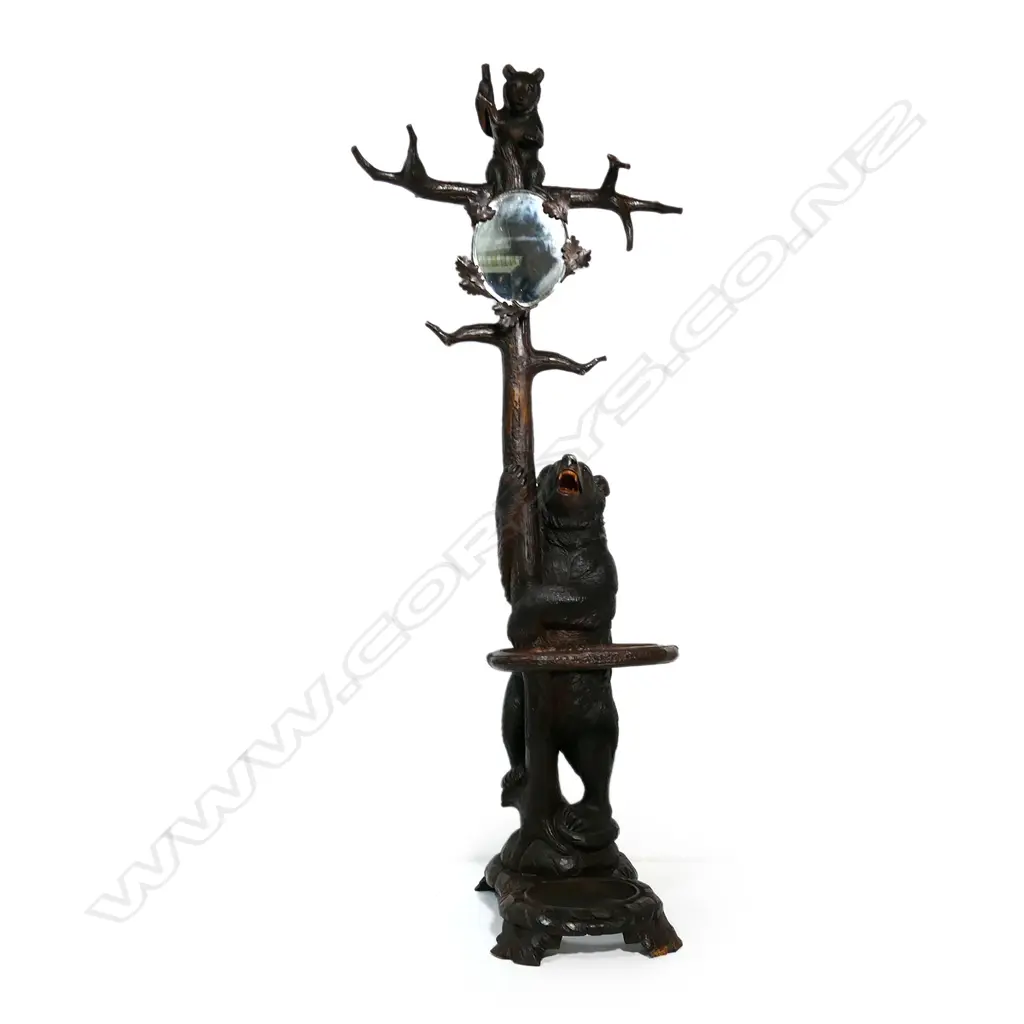 An early 1900s carved Black Forest bear hall/umbrella stand, the mother bear holding the tree trunk and with her cub perched on the top, oak leaf framed mirror to the centre, some evidence of old borer to the right hand side of the base, drip tray absent. (Together with a copy of 'Swiss Carvings, The Art of the Black Forest' which features this design in the chapter on hallstands.) 770 x 540 x 2050mm. Image 1++