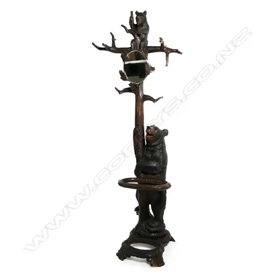 An early 1900s carved Black Forest bear hall/umbrella stand, the mother bear holding the tree trunk and with her cub perched on the top, oak leaf framed mirror to the centre, some evidence of old borer to the right hand side of the base, drip tray absent. (Together with a copy of 'Swiss Carvings, The Art of the Black Forest' which features this design in the chapter on hallstands.) 770 x 540 x 2050mm.