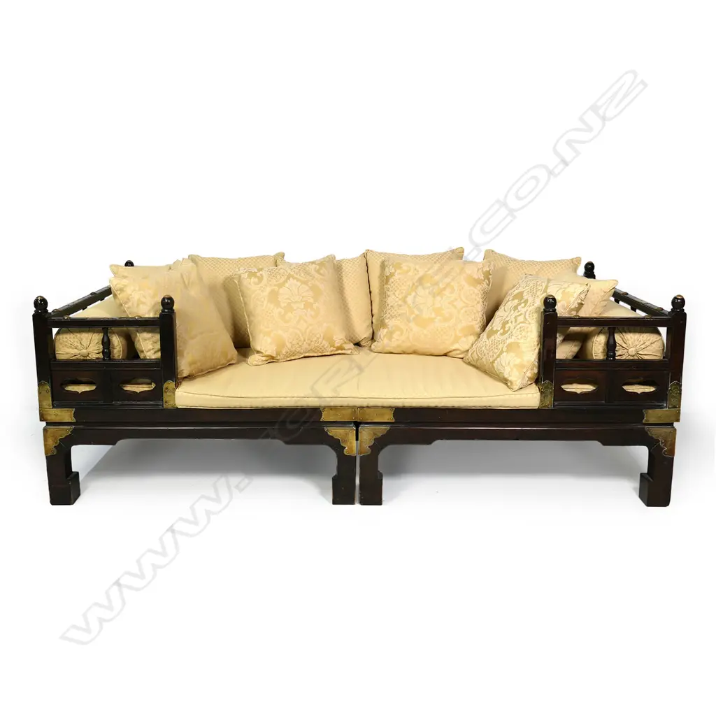 A vintage Chinese hardwood opium bed, the frame with brass embellishments and corner strappings, with one long seat cushion, three bolster pillows and ten small pillows, upholstered in a gold self-patterned brocade.  2030 x 1010 x 700mm. Image 1++