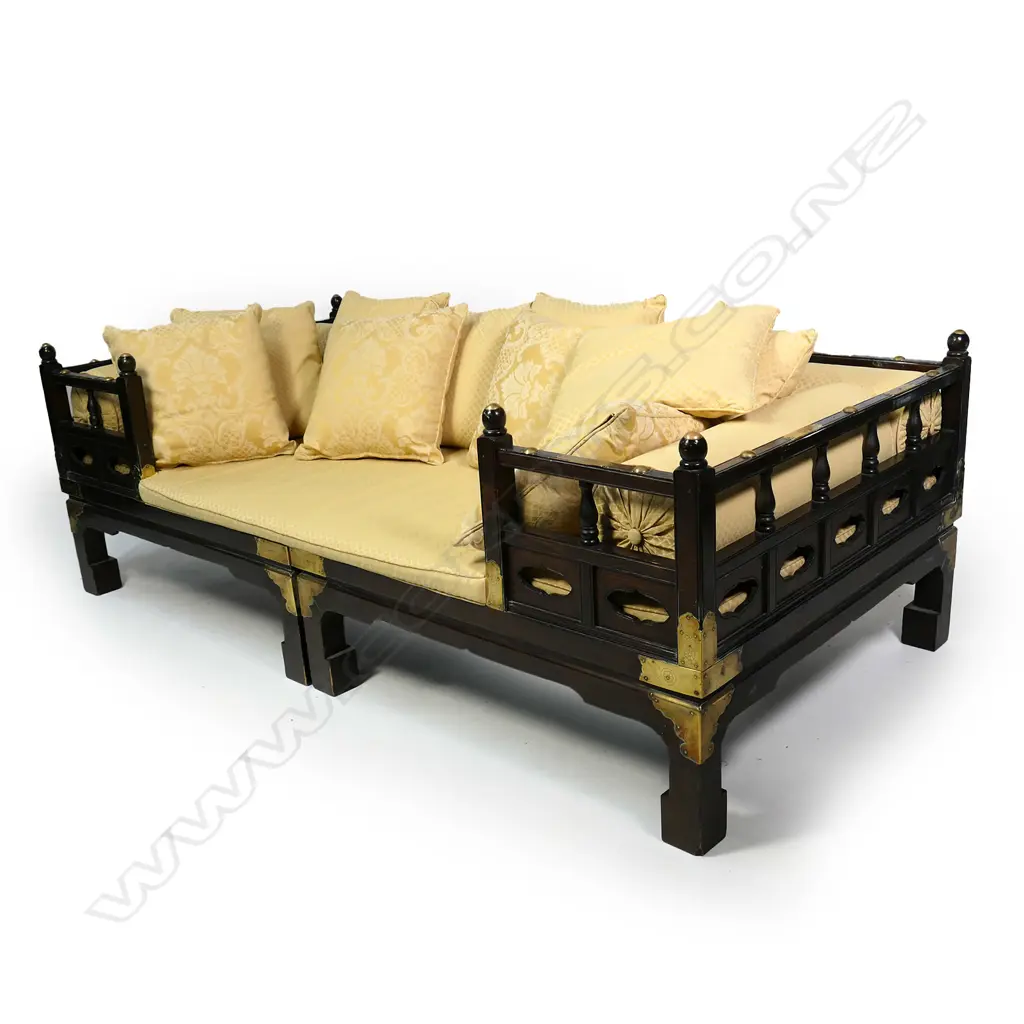 A vintage Chinese hardwood opium bed, the frame with brass embellishments and corner strappings, with one long seat cushion, three bolster pillows and ten small pillows, upholstered in a gold self-patterned brocade.  2030 x 1010 x 700mm. Image 1++