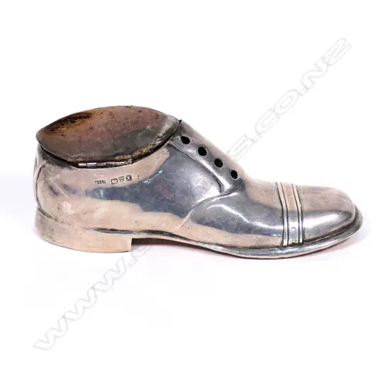 An Edwardian silver pin cushion, in the form of the gentleman's shoe, the pin cushion lifts to reveal a small cavity beneath, some damage to the cushion, Chest 1910. L.125mm. Original oak base.