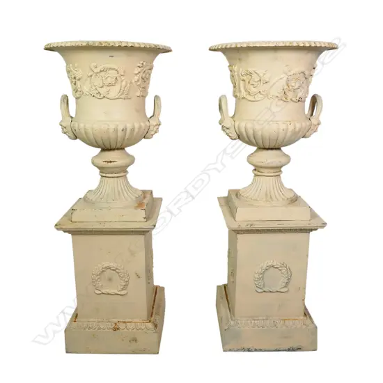 A pair of cast iron garden urns on plinths,