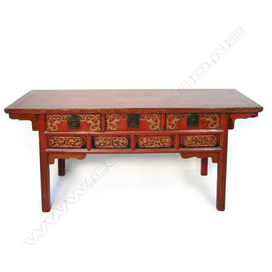 A large red lacquer Chinese side table, with three frieze drawers with raised gilded decorative carving above an apron with further gilded decoration,